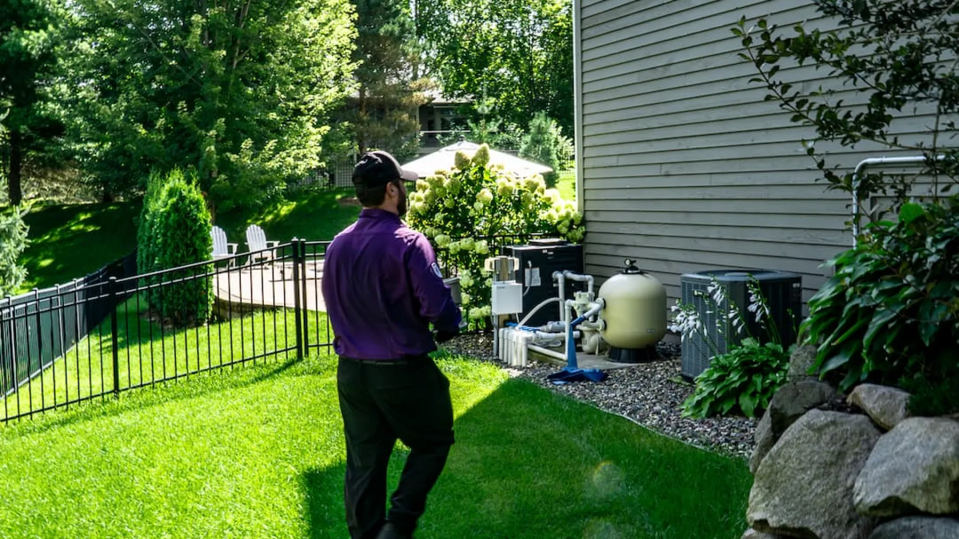 Technician inspecting pool equipment setup outside a house on a sunny day with green lawn and trees