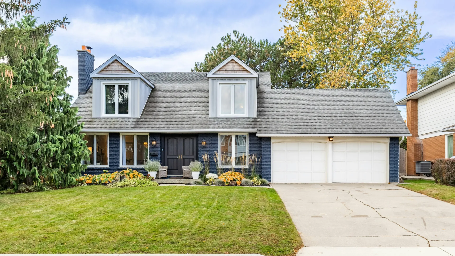 Two-story suburban home with gray roof, black brick walls, large green lawn, and double garage under a blue sky.