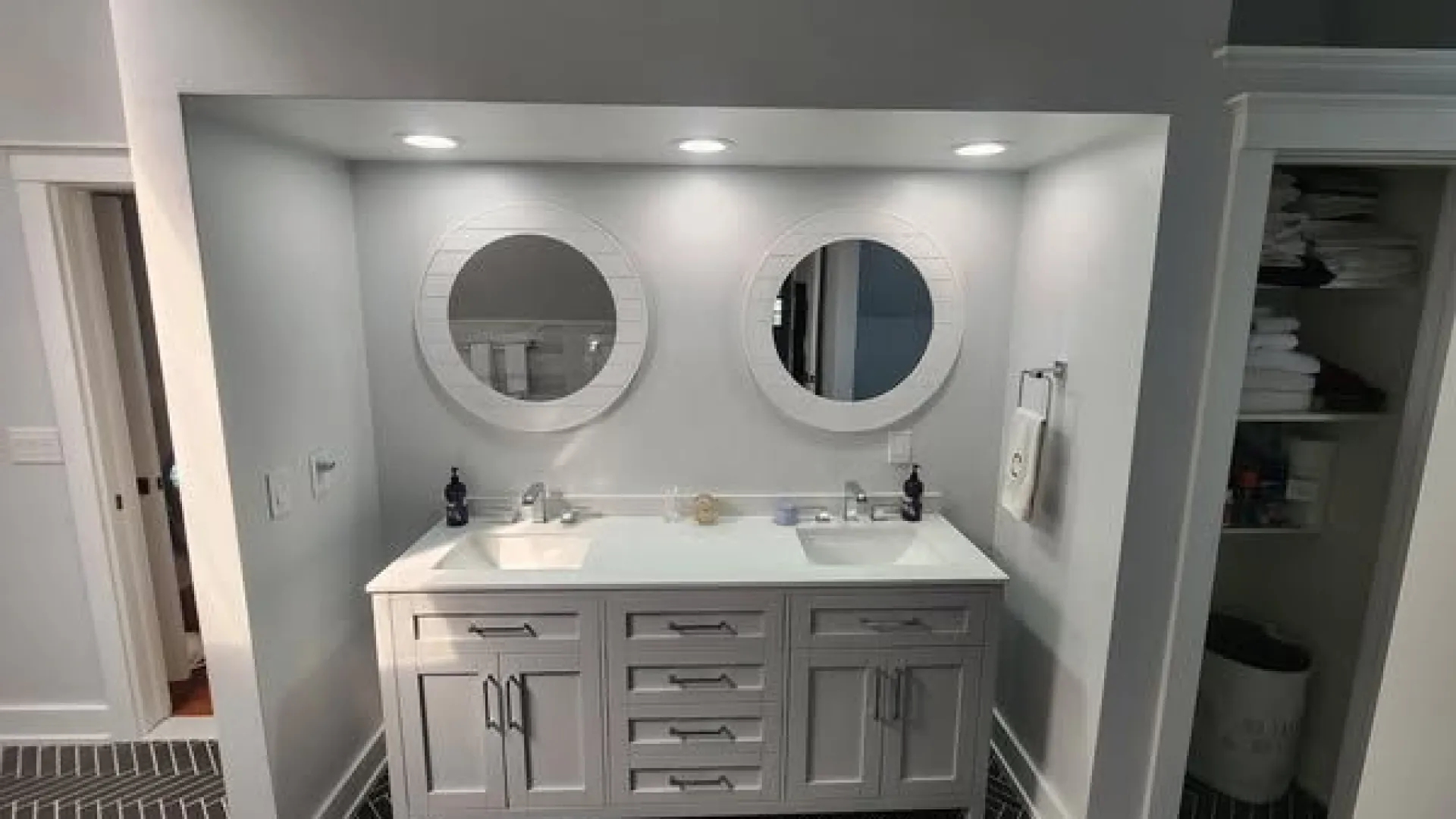 Modern bathroom double vanity with white round mirrors, gray cabinet, and dark herringbone floor tiles.