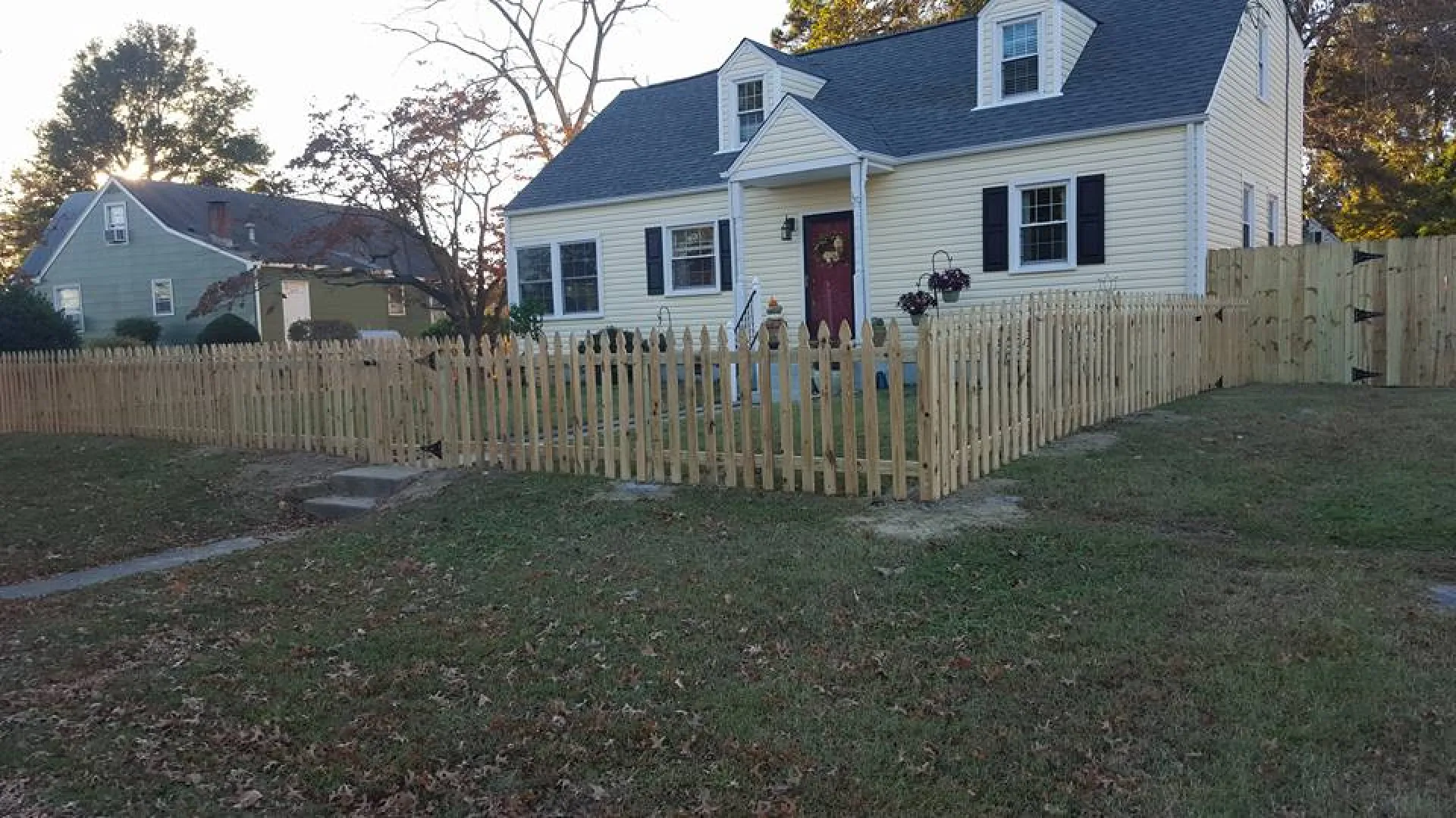 White house with a dark roof surrounded by a newly installed wooden picket fence on a grassy yard.