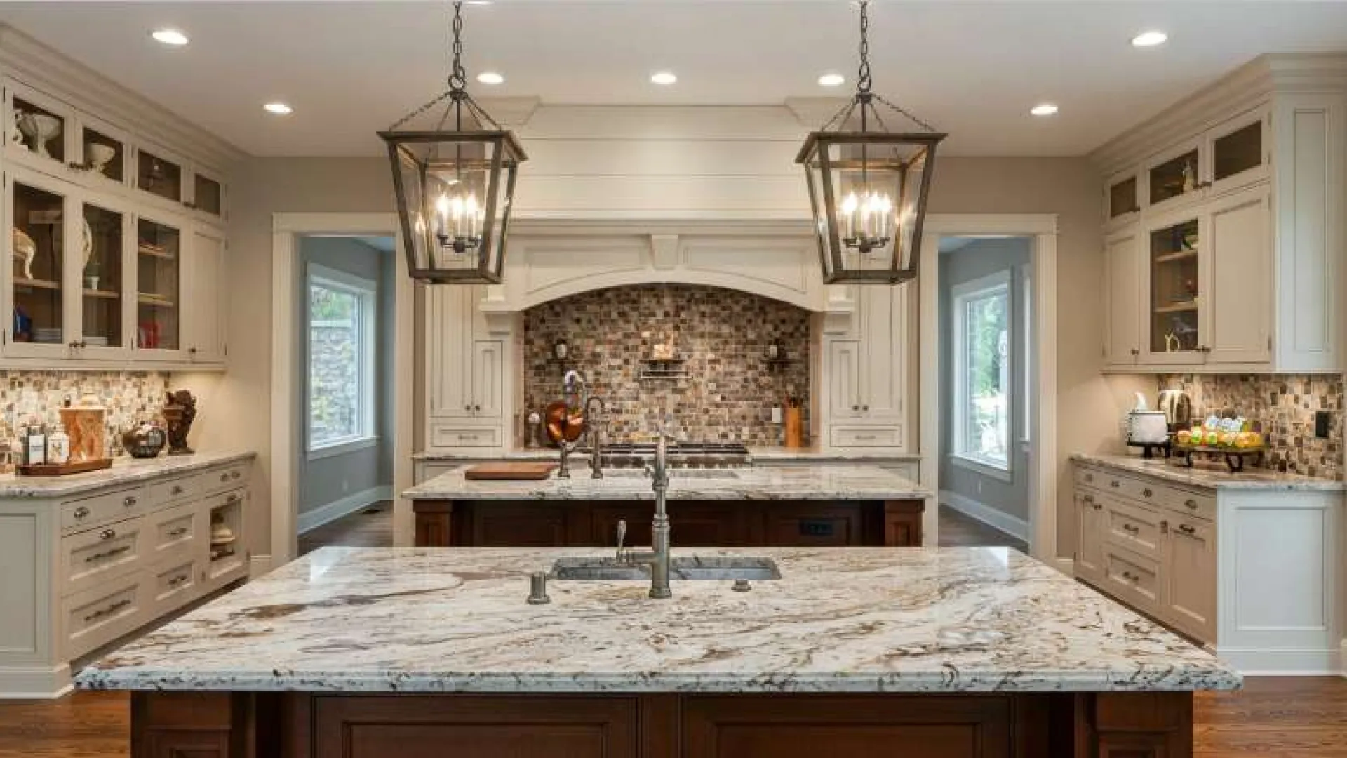 Spacious modern kitchen with marble countertops, beige cabinetry, pendant lighting, and mosaic tile backsplash.