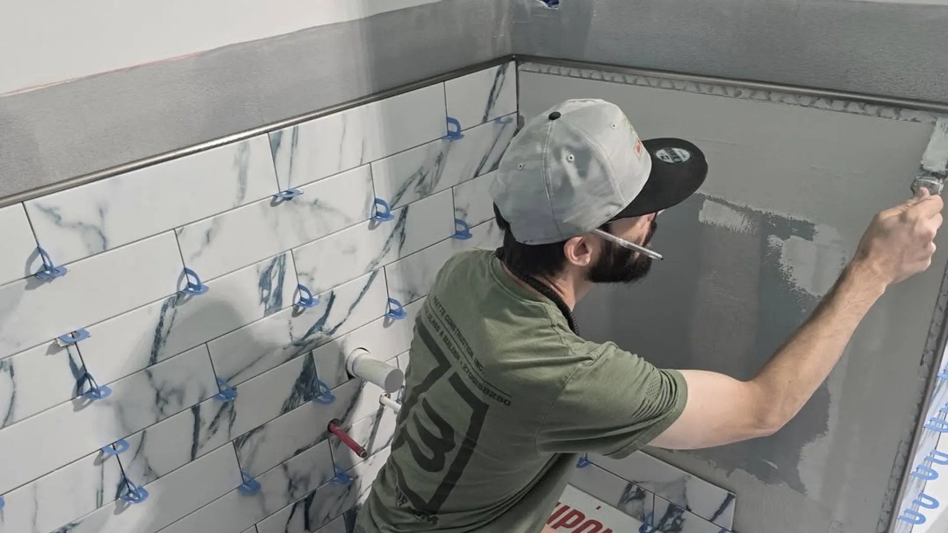 Man installing marble-patterned wall tiles and applying adhesive in a bathroom renovation project.