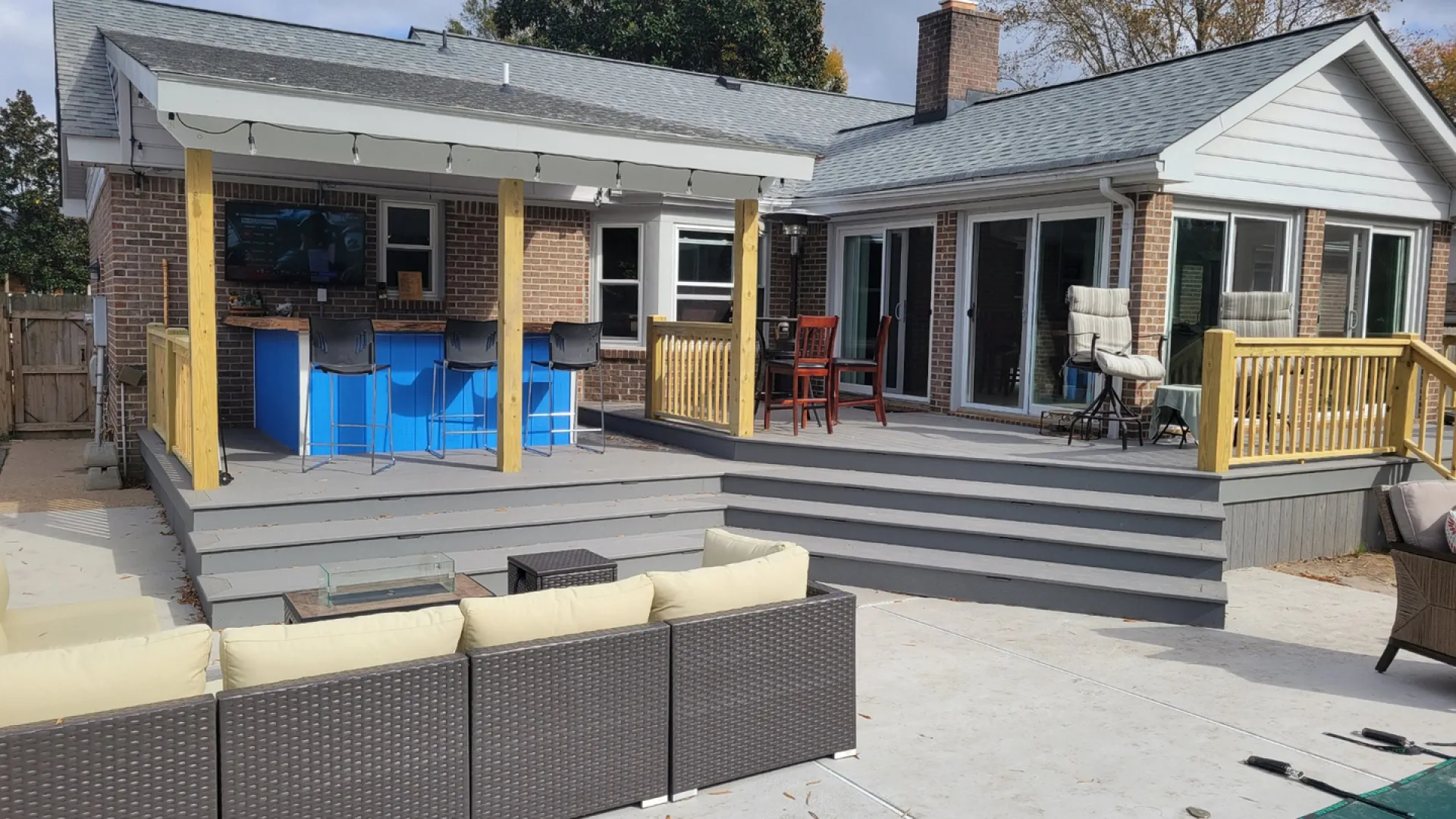 Spacious backyard deck with outdoor bar, seating area, and modern patio furniture beside a brick house.
