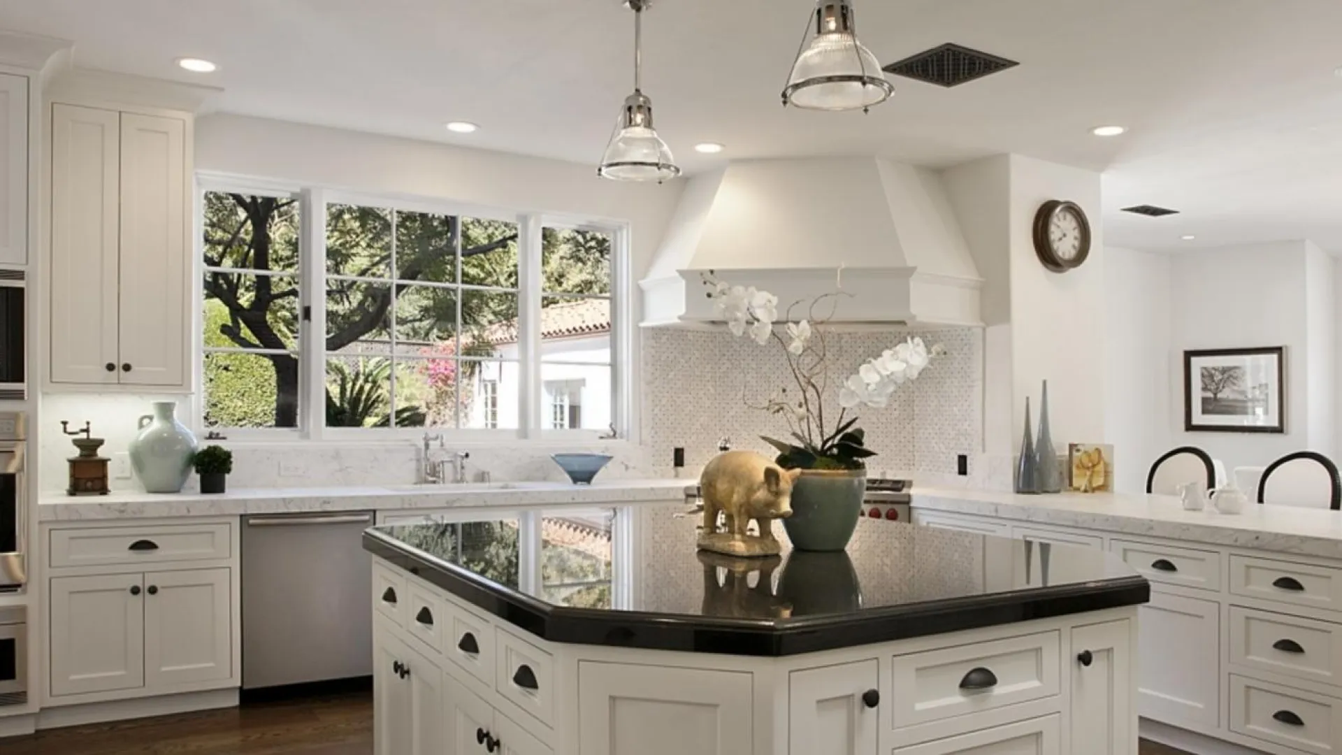 Modern spacious kitchen with white cabinets, black granite island countertop, stainless steel appliances, and large windows.
