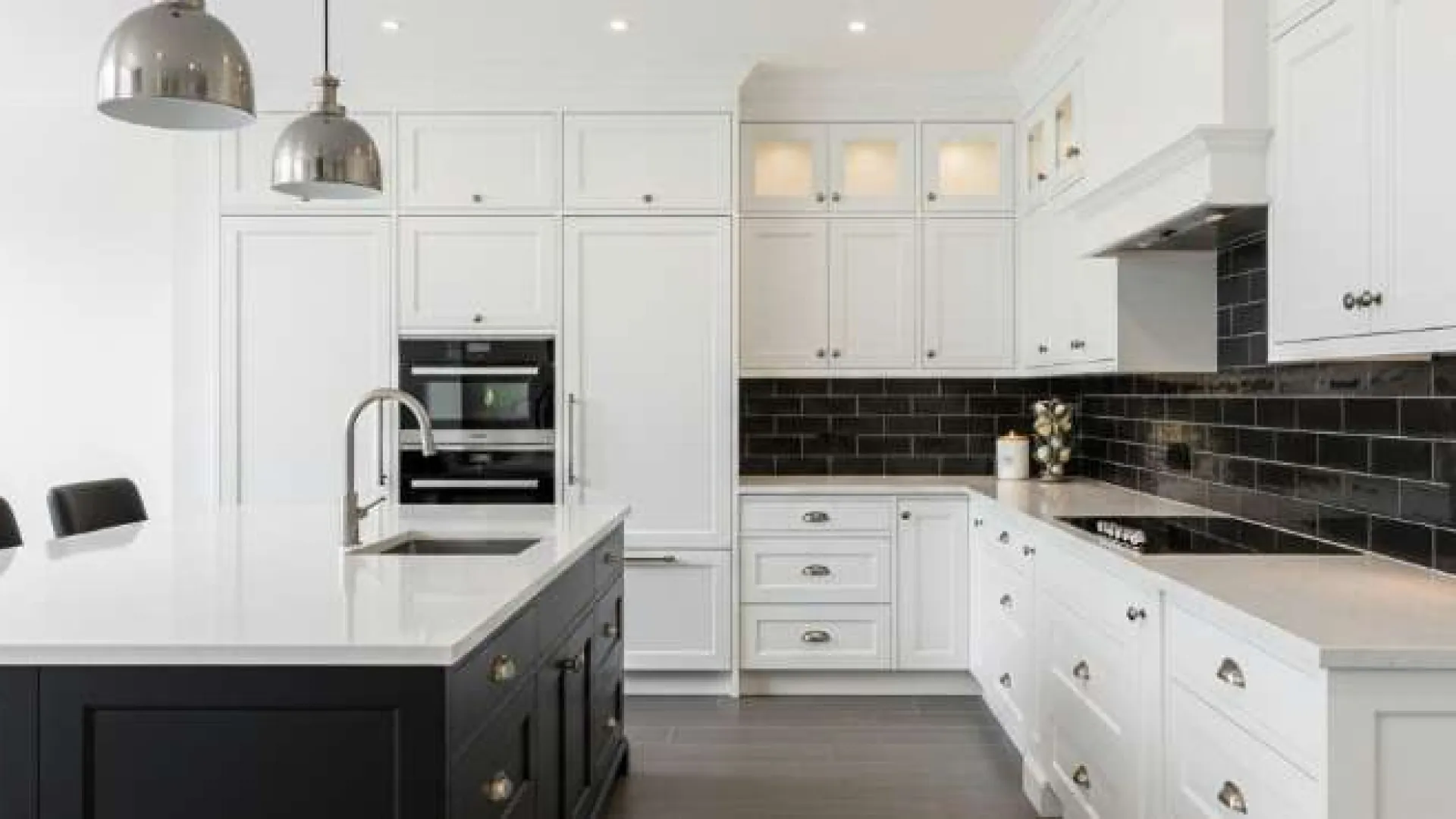 Modern kitchen with white cabinetry, black subway tile backsplash, large island with sink, and pendant lights