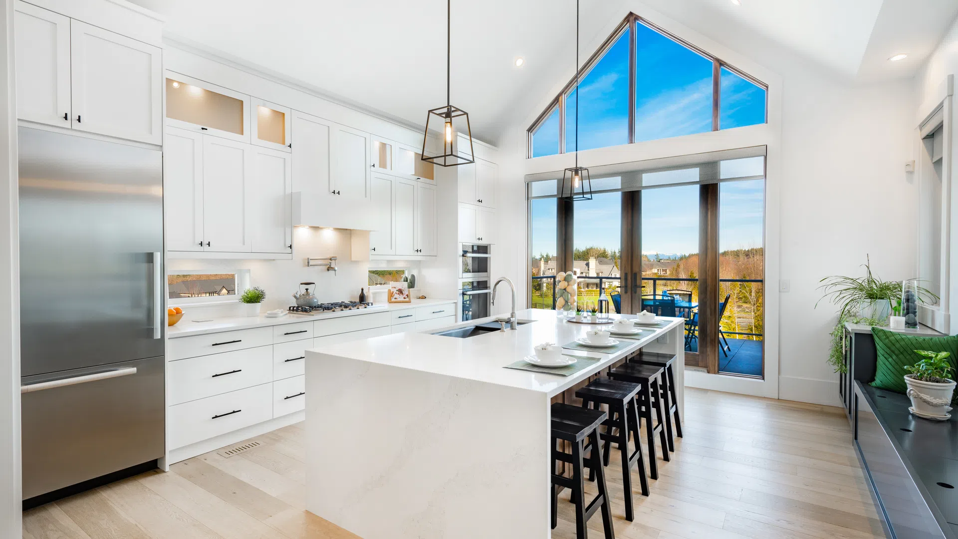 Bright modern kitchen with white cabinetry, large island, bar stools, stainless steel appliances, and large windows with balcony view.