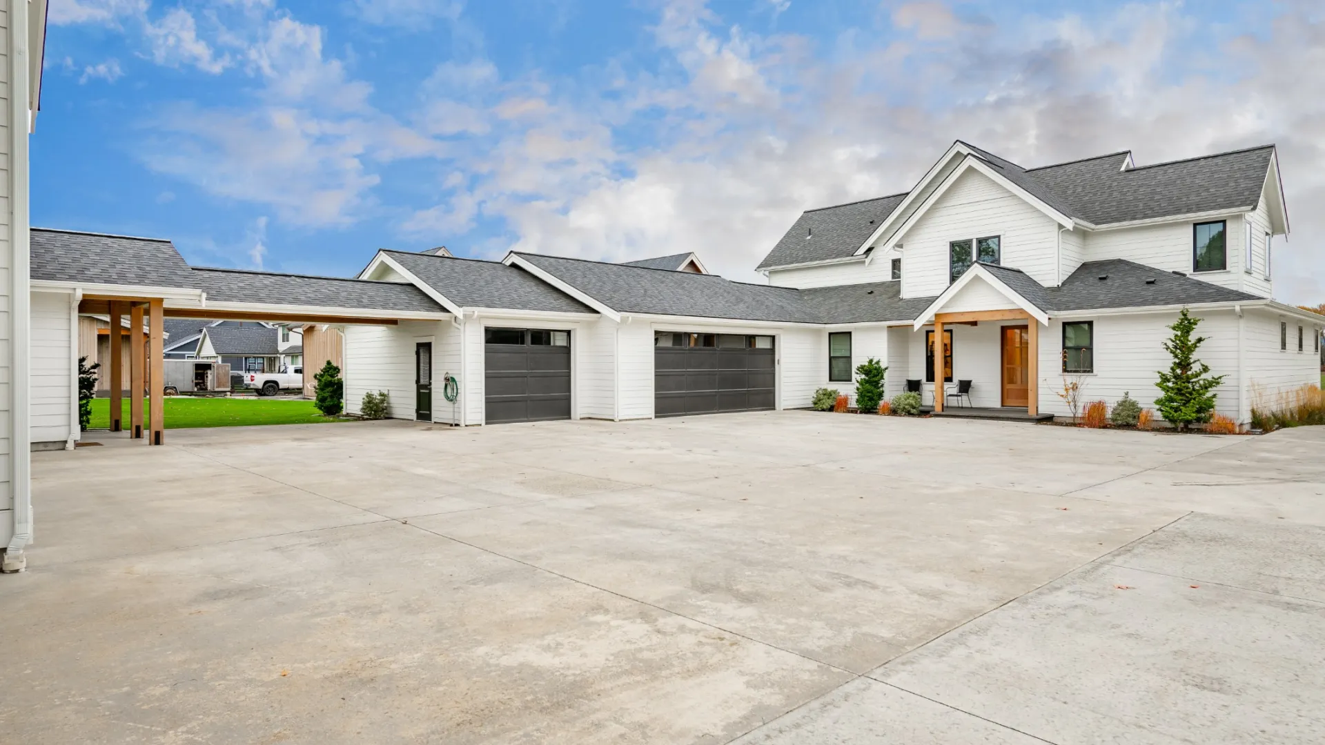 Modern white two-story house with multiple garages and spacious concrete driveway under a blue sky.