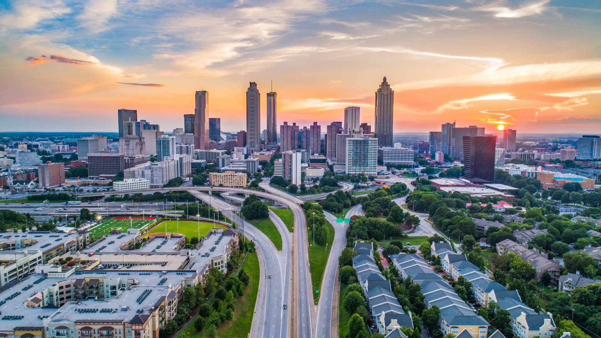 Aerial view of Atlanta skyline during sunset with vibrant clouds and busy highways.