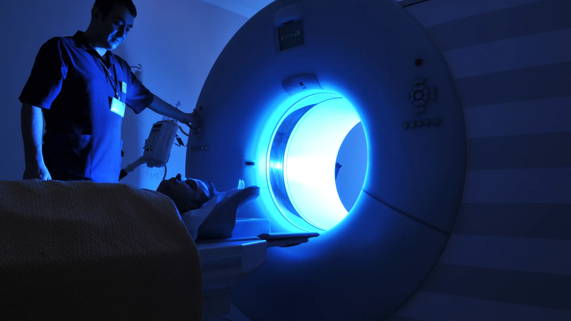 Medical technician operating a glowing MRI machine in a dimly-lit room.