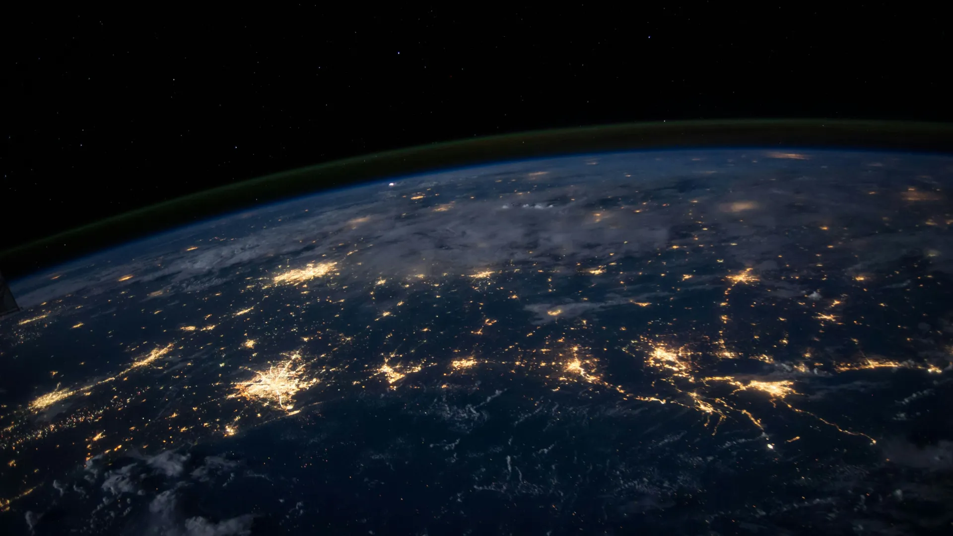 Earth viewed from space at night showing illuminated cities and dark surrounding oceans and skies.
