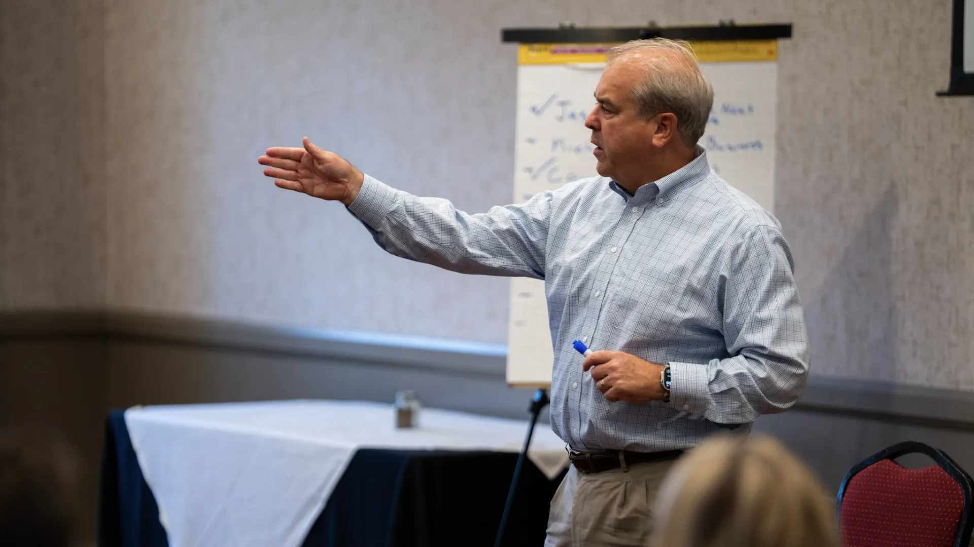 Man in dress shirt giving a presentation using a flip chart in a conference room with seated audience.