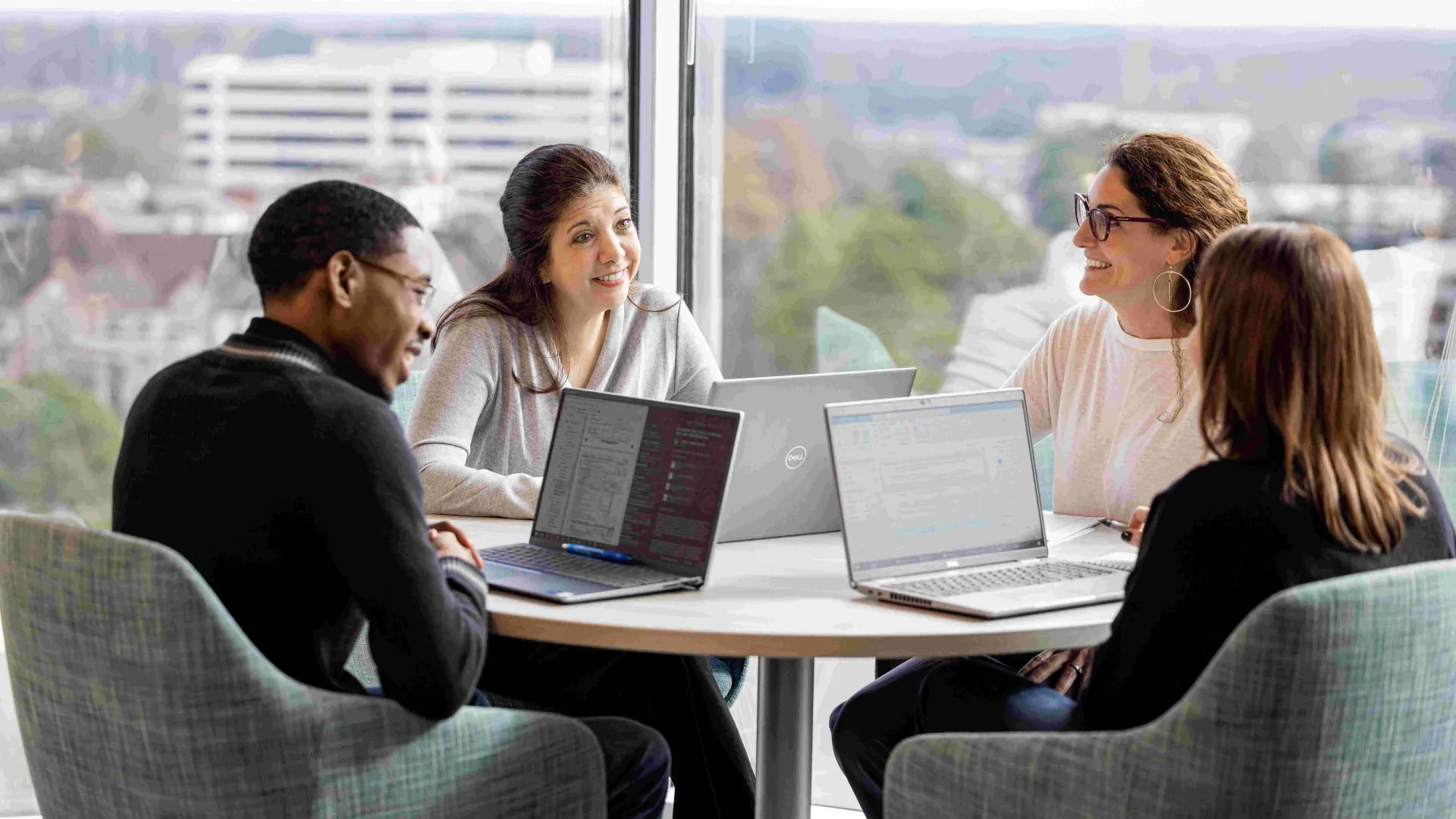 a group of people sitting around a table with laptops