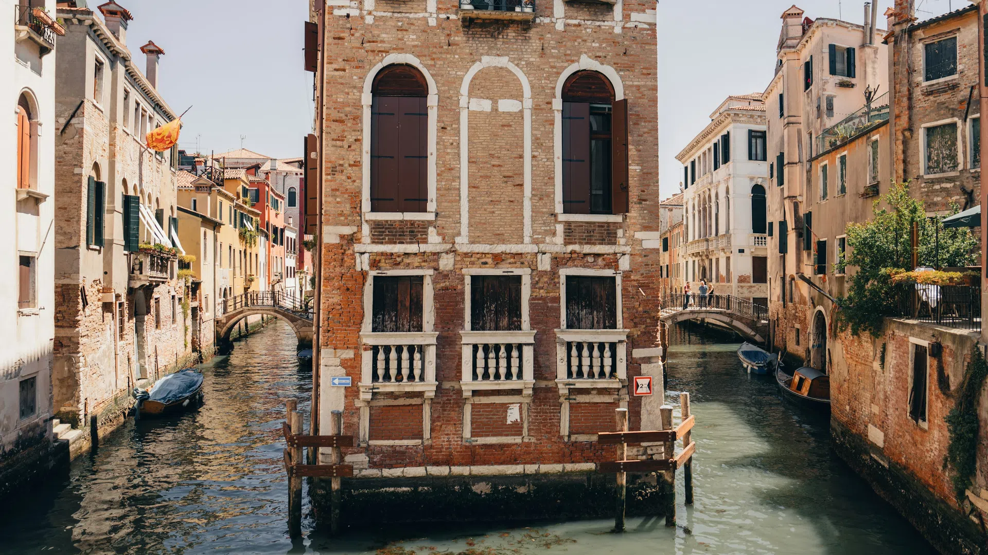 Historic brick building at canal junction with arched windows and boats in Venice, Italy waterways.
