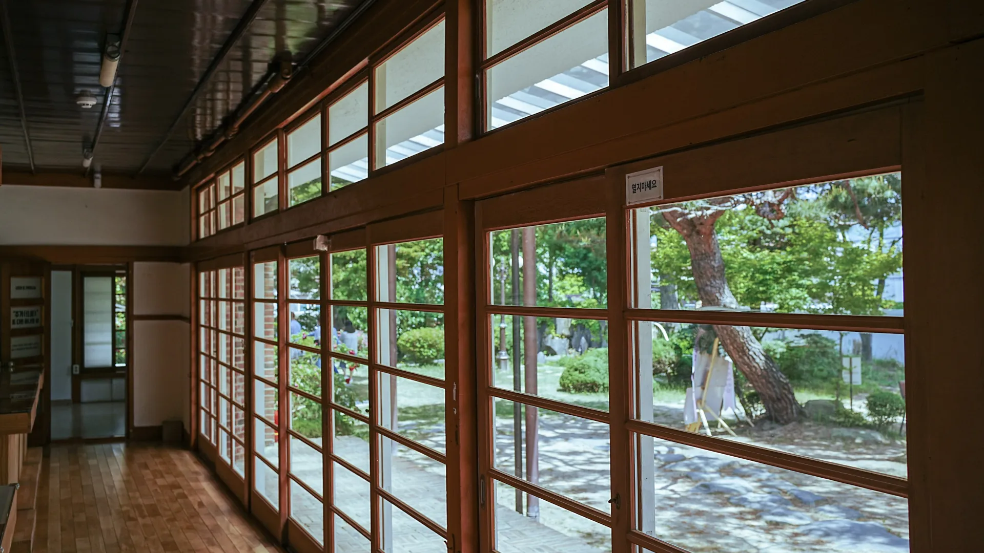 Interior of a traditional Japanese building with wooden floors and large shoji-style windows overlooking a garden.