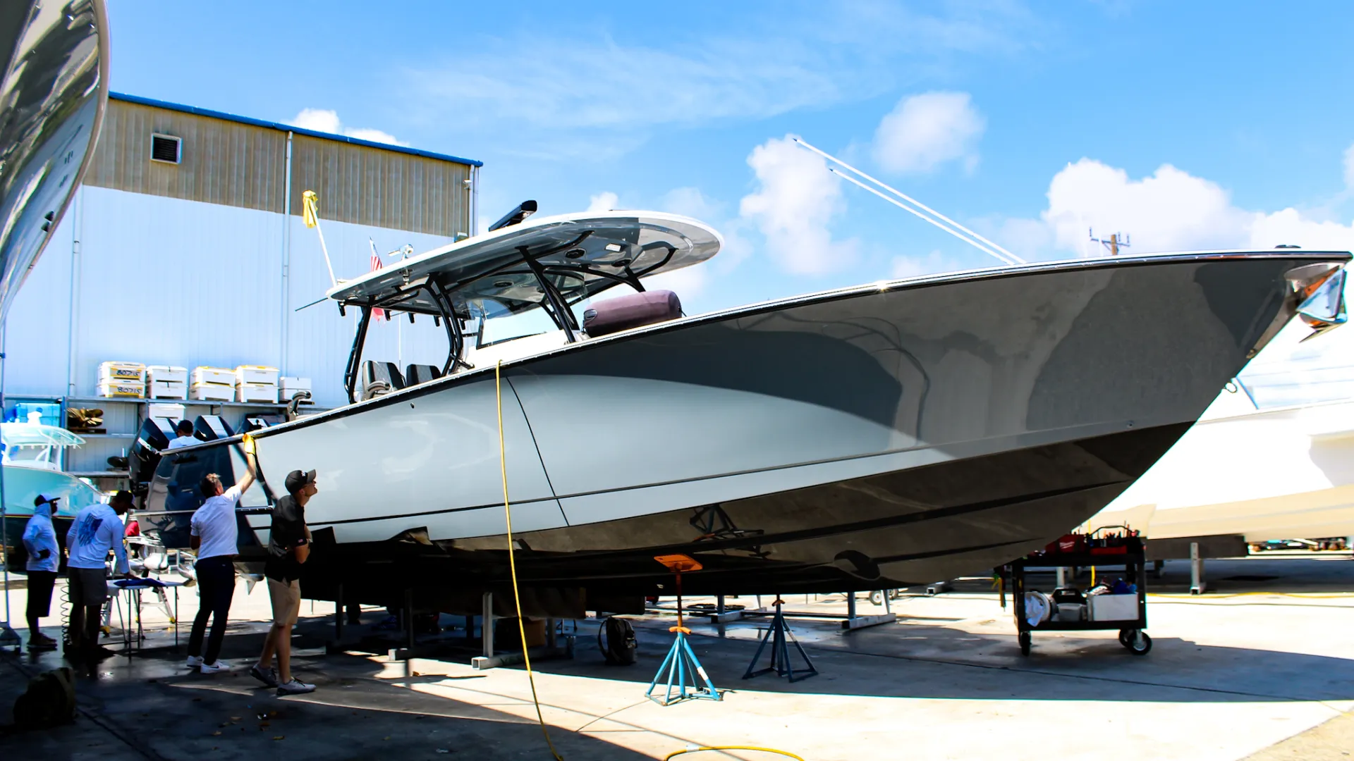 Large sleek black and white powerboat on dry dock with workers and equipment under clear blue sky.