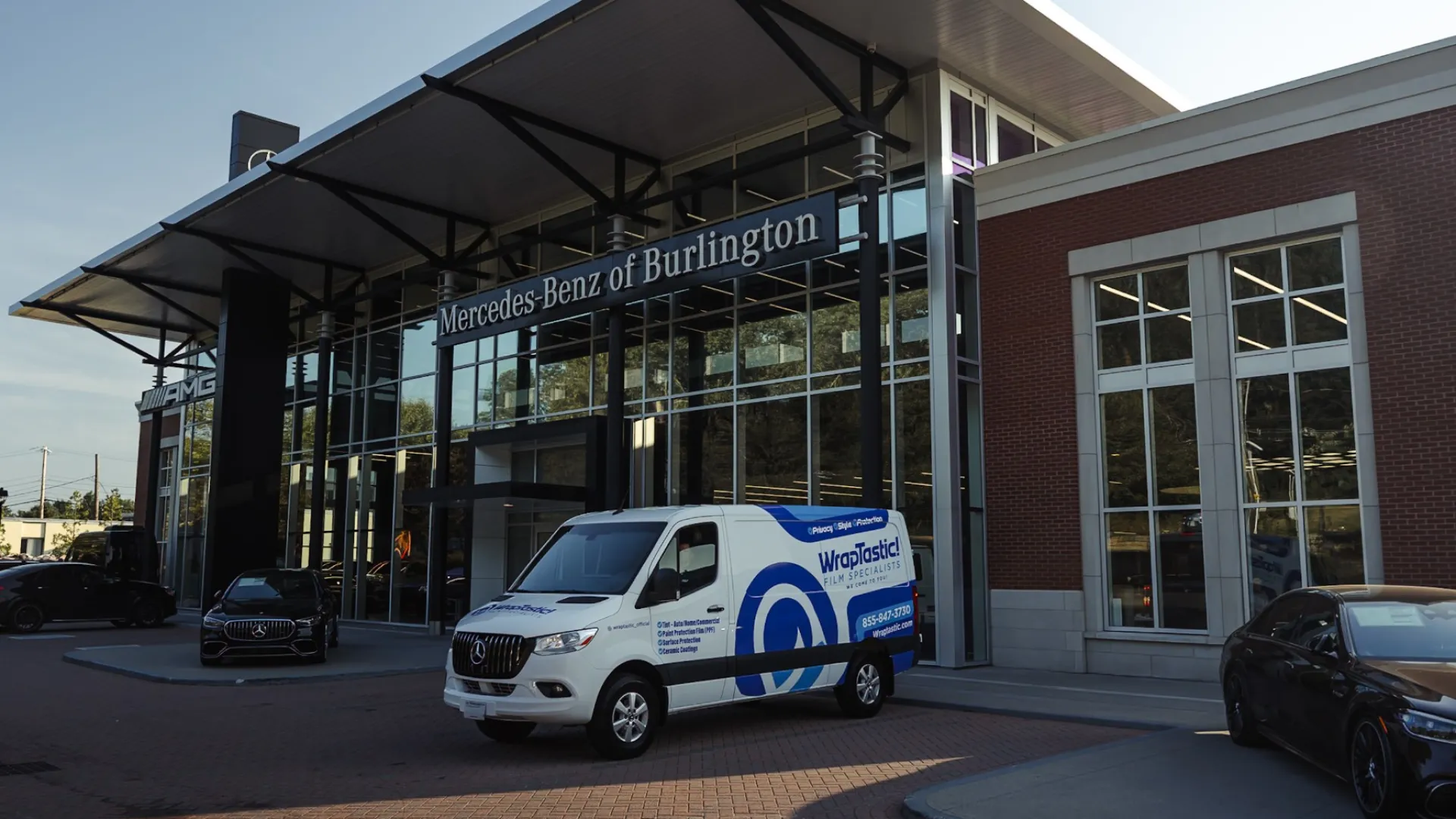White WrapPlastics van parked in front of Mercedes-Benz of Burlington dealership with luxury cars and modern building