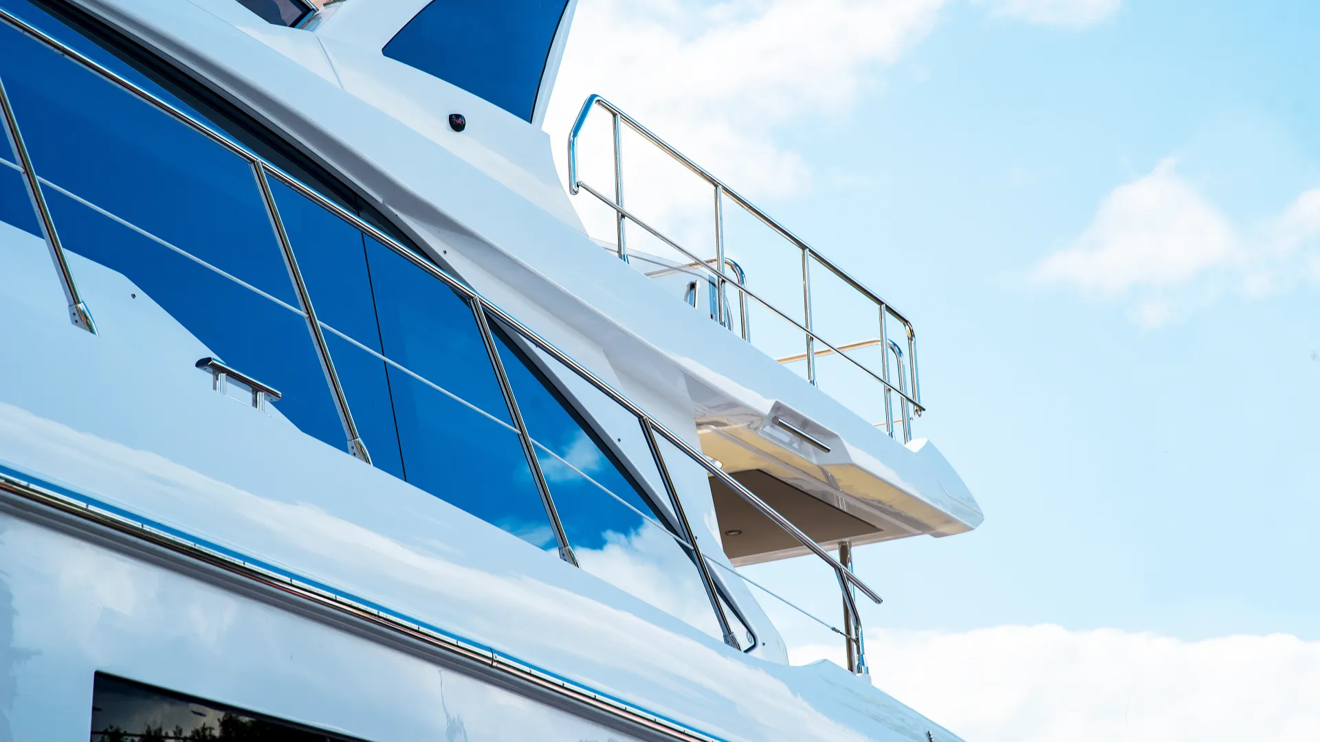 Close-up of a modern white yacht with reflective blue windows against a bright sky with clouds.