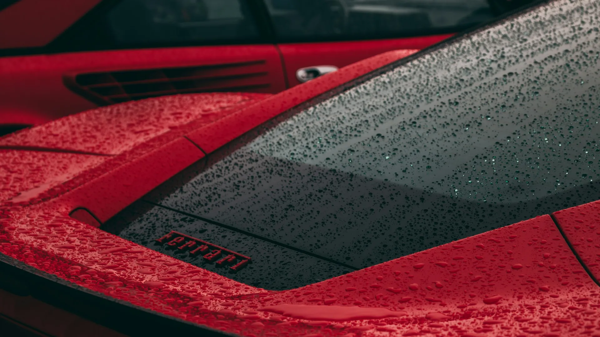 Close-up of red Ferrari cars with rain droplets on the surface highlighting the sleek design and logo.