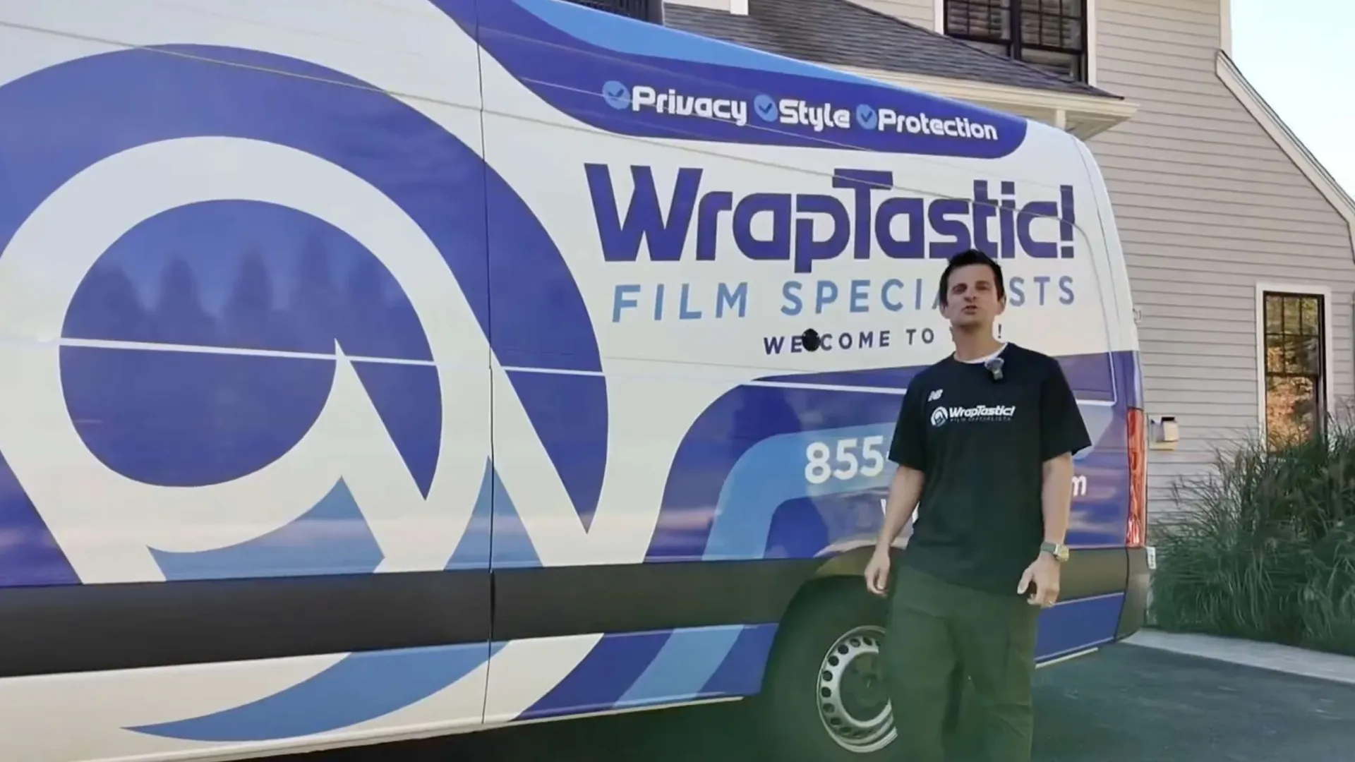 Man stands beside a Wraptastic van featuring blue and white branding for window film specialists outside a house.
