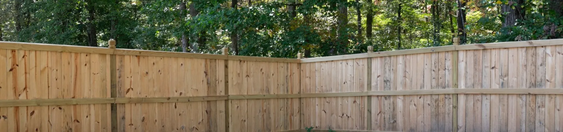 Wooden fence enclosing a natural green space surrounded by trees in a peaceful woodland setting.