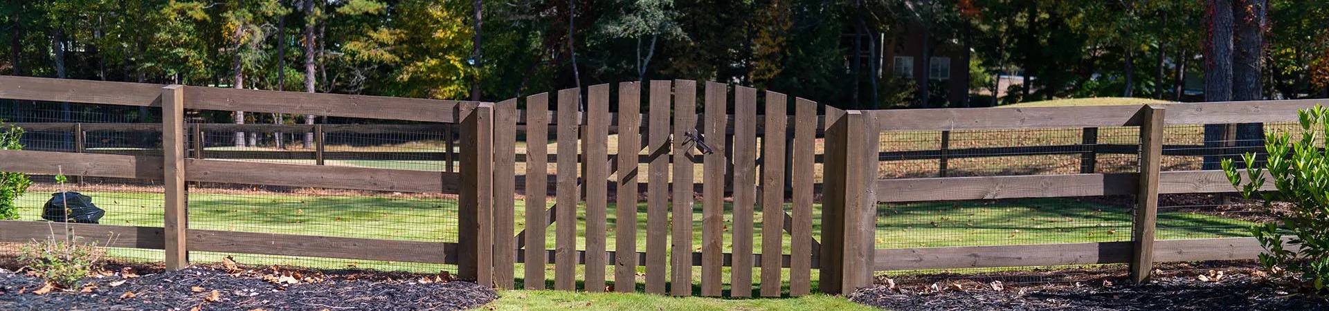 a fenced in yard with a wood gate and trees in the background