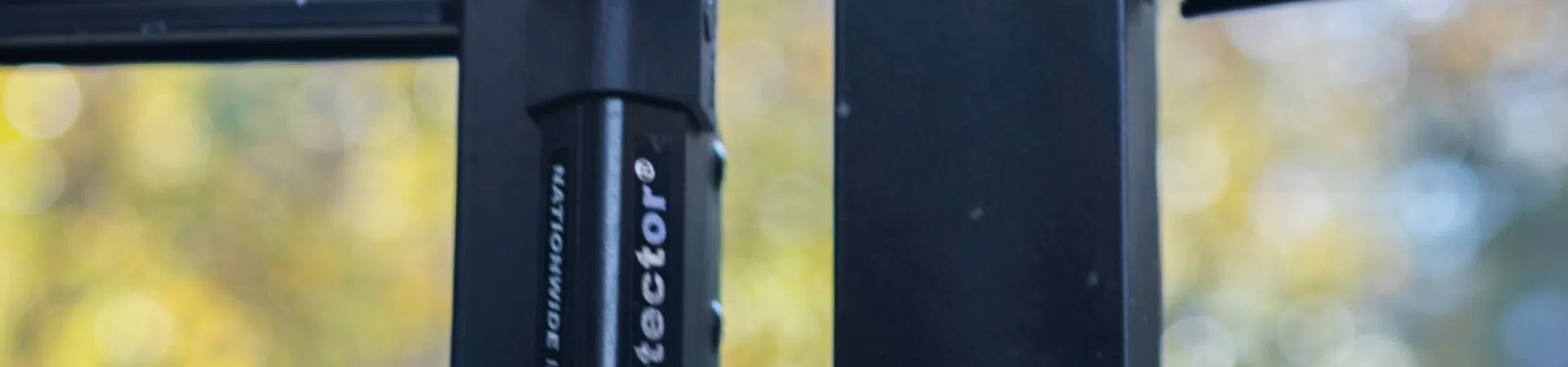 Close-up of a black gate latch with bright blue screw against a blurred outdoor background.