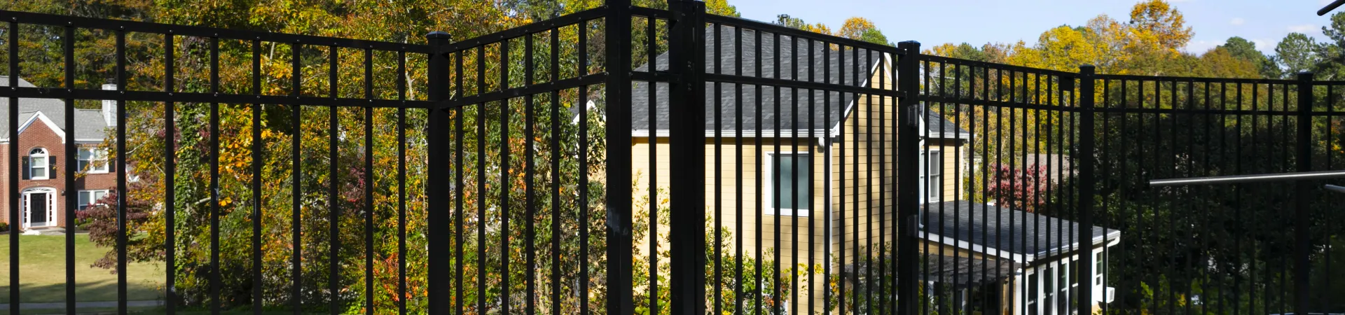 Black metal fence surrounding a backyard with a green lawn and colorful autumn trees.