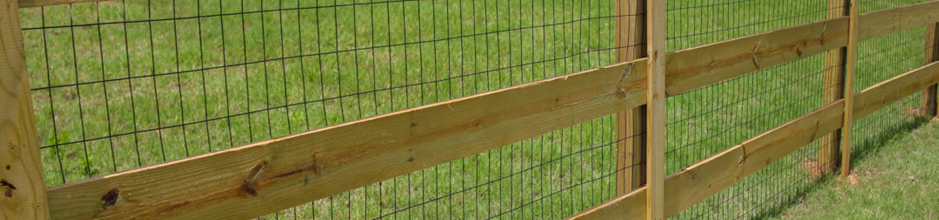 Wood and wire garden fence enclosing a green backyard with grass and houses in the background.