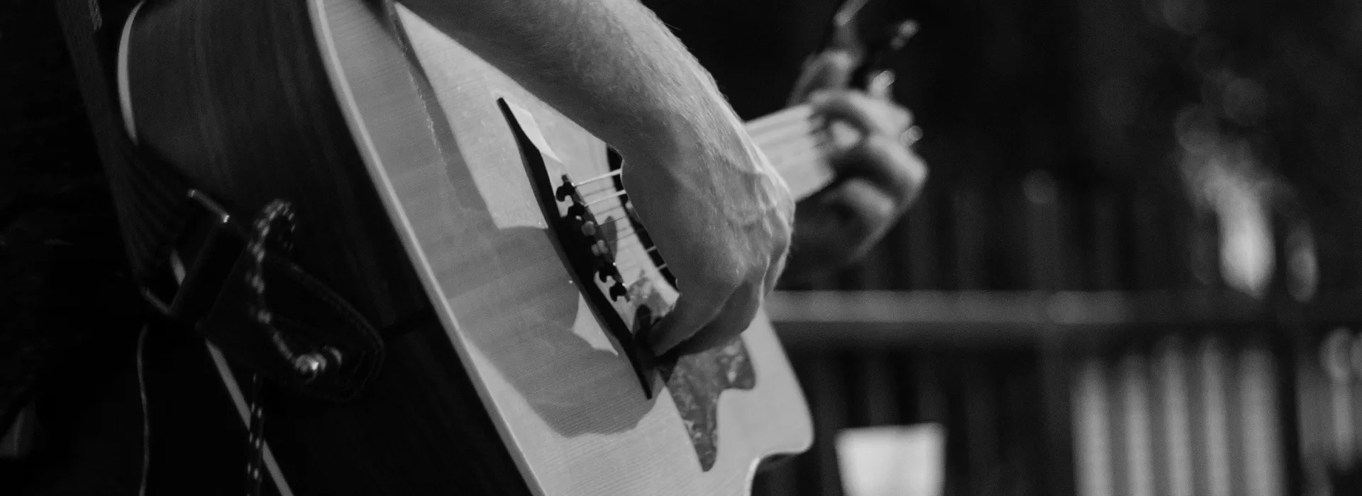 Black and white close-up of hands playing an acoustic guitar with blurred background