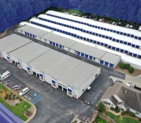 Aerial view of a self-storage facility with multiple white buildings and rows of storage units surrounded by greenery.