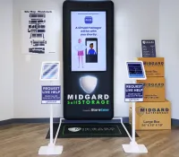 Self-storage kiosk with virtual manager screen, request live help tablets, and stacked Midgard storage boxes in office lobby.