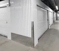 Indoor storage facility corridor with white roll-up metal doors and concrete floor under fluorescent lighting