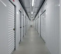 Indoor corridor with rows of white storage unit doors secured with locks in a self-storage facility.