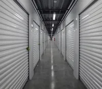 Long corridor of indoor storage units with closed white roll-up doors and polished concrete floor.