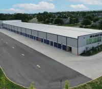 A large self-storage facility with multiple blue doors, surrounded by paved roads and nearby residential homes.