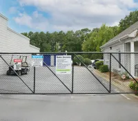 Black metal security gate with warning signs blocks entrance between two white buildings with greenery