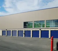 Modern self-storage facility with closed blue roll-up doors and large tinted windows under clear sky.