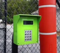Bright green keypad access control box mounted next to a red column in an outdoor fenced area.