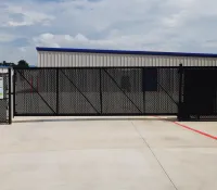 Black metal security gate with access instructions in front of a storage facility building under a cloudy sky.
