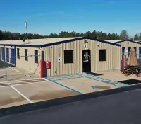 Storage facility with beige metal buildings, blue roll-up doors, fenced area, and a picnic table with umbrella