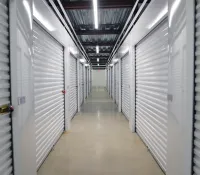 Long corridor with closed white metal storage unit doors and bright overhead lighting in a clean storage facility.