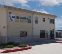 Midgard Self Storage facility building with signage under blue sky and parking area in front.