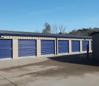Outdoor row of storage unit garages with blue roll-up doors under a clear sky on concrete pavement.