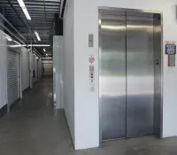 Stainless steel elevator in a clean storage facility hallway with metal roll-up doors and concrete floor.