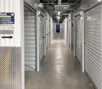 Indoor hallway of a self-storage facility with rows of closed, gray roll-up metal doors and concrete floor.
