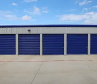 Row of blue storage unit doors with concrete driveway under a partly cloudy sky