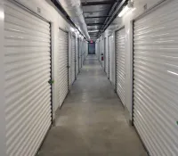 Long hallway of a modern storage facility with white metal roll-up doors and concrete floor