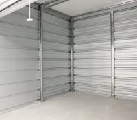 Empty indoor storage unit with gray metal walls and concrete floor, open roll-up door visible overhead.