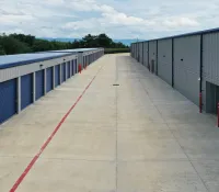 Outdoor storage facility with rows of blue roll-up doors and wide concrete driveway under cloudy sky.