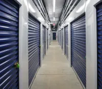Interior view of a clean storage facility corridor with blue roll-up doors secured with locks.